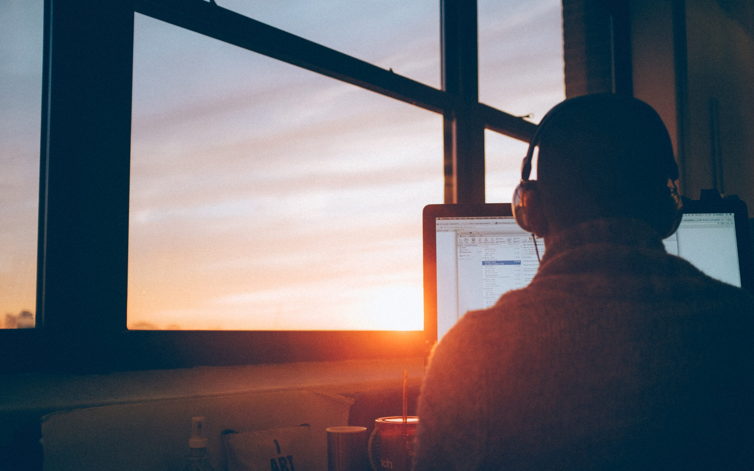 Person from behind sitting on computer with headphones on